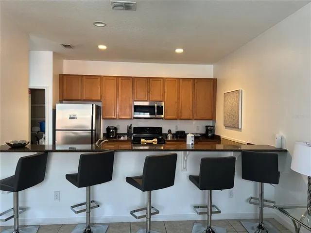 a kitchen with stainless steel appliances granite countertop a stove a sink a refrigerator and chairs