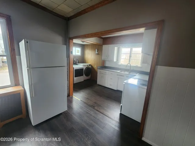 a view of a refrigerator in kitchen and an empty room with wooden floor windows