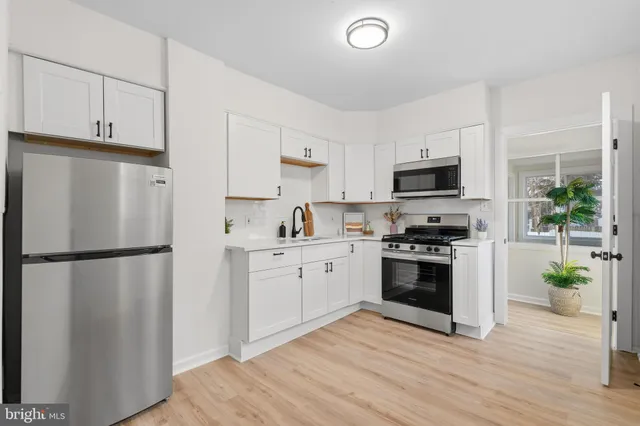a white kitchen with stainless steel appliances a refrigerator a stove a sink a microwave and cabinets