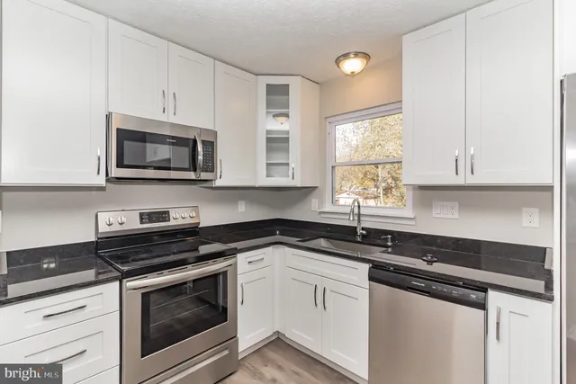 a kitchen with granite countertop white cabinets appliances a window and a sink