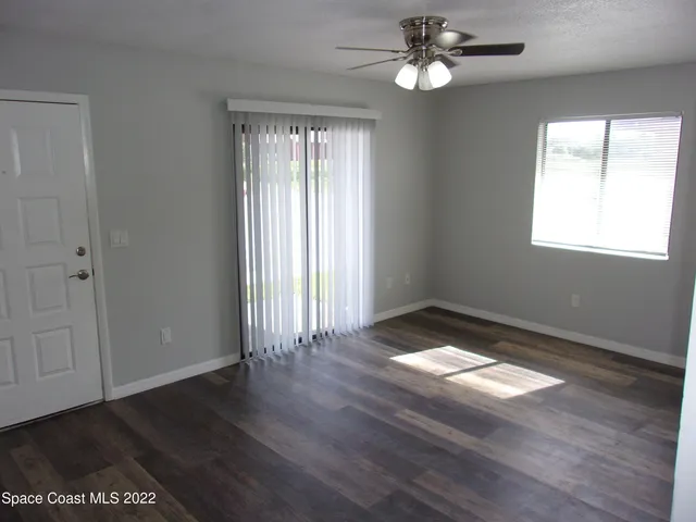 an empty room with wooden floor chandelier fan and windows