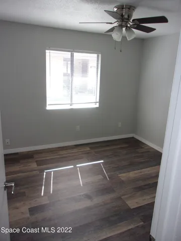 an empty room with wooden floor fan and windows
