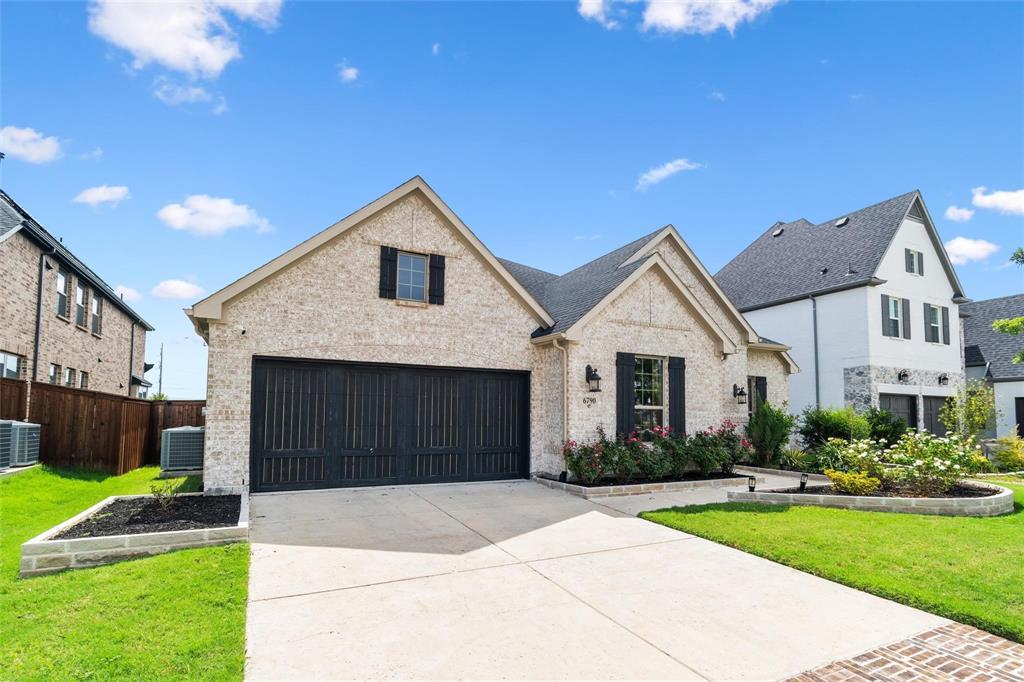 French country inspired facade featuring concrete driveway, a front yard, brick siding, and fence