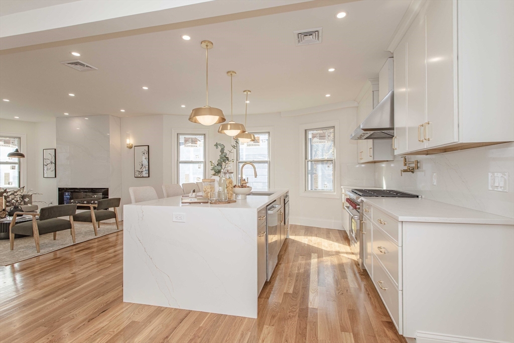 125 Mt Vernon Street, Unit 2 Newton, MA 02465 - Photo 8 of 36 a large kitchen with kitchen island a stove a sink a refrigerator and a dining table with wooden floor
