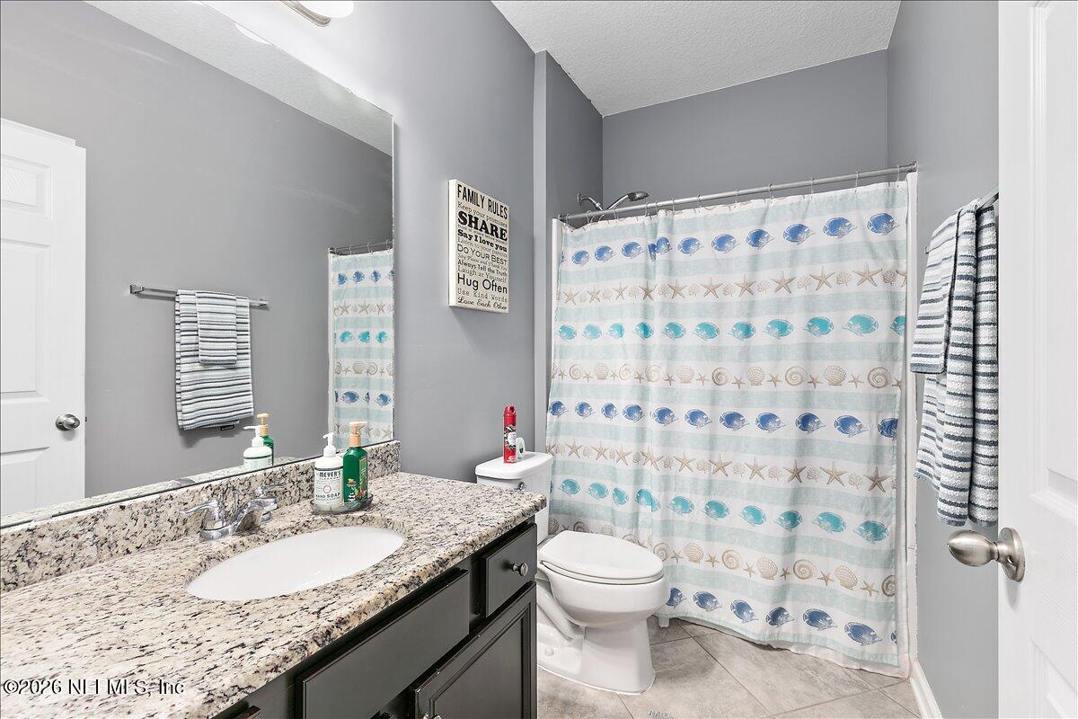 53 Monroe Avenue St. Augustine, FL 32086 - Photo 20 of 26 a bathroom with a granite countertop sink a toilet a mirror and shower curtain