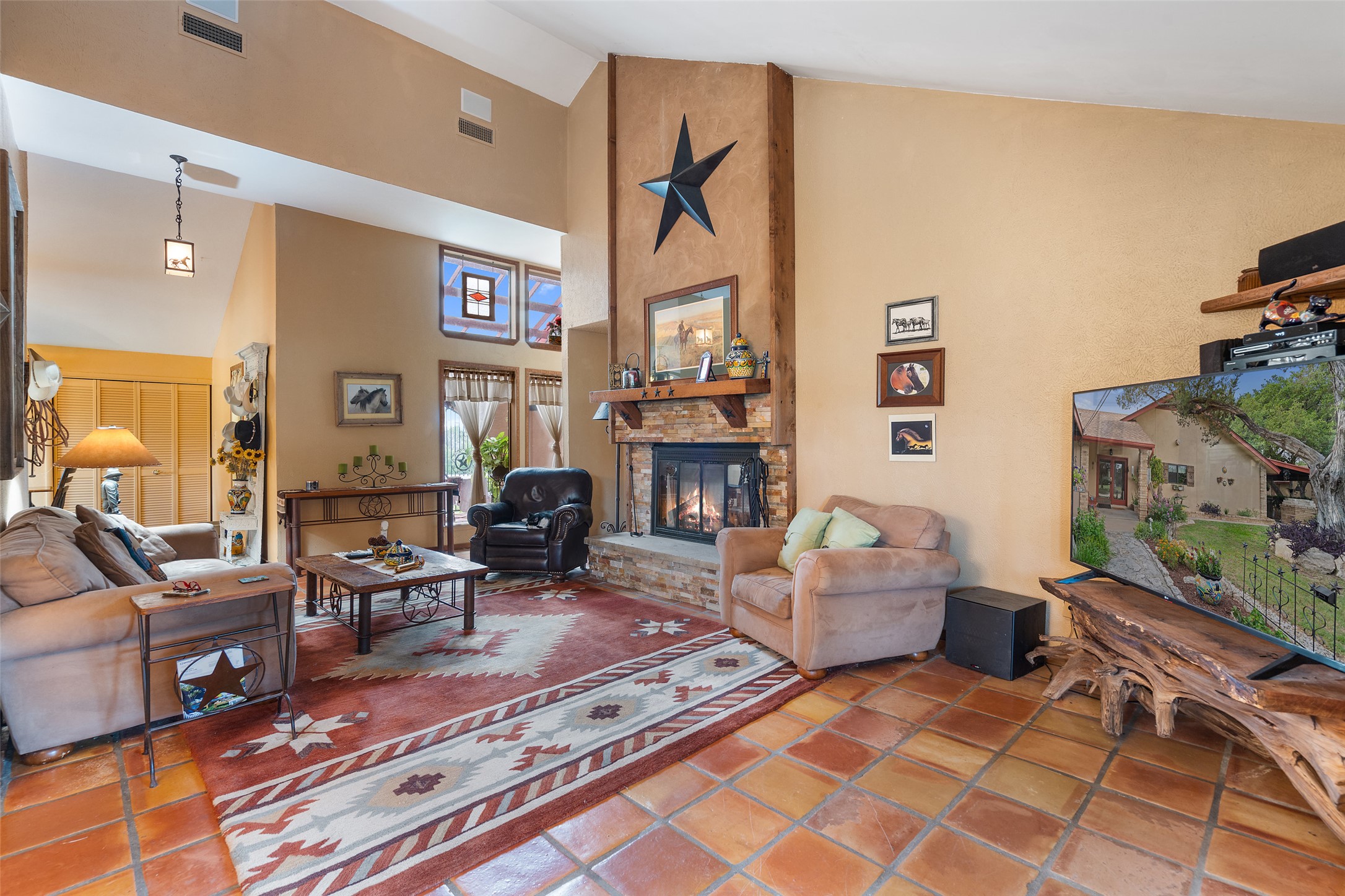 23200 Fulkes Road Leander, TX 78641 - Photo 5 of 15 A spacious living area showcasing a grand stone fireplace with vaulted ceilings and rich terracotta flooring.