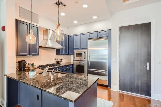 a kitchen with stainless steel appliances granite countertop a sink a refrigerator and a wooden floor