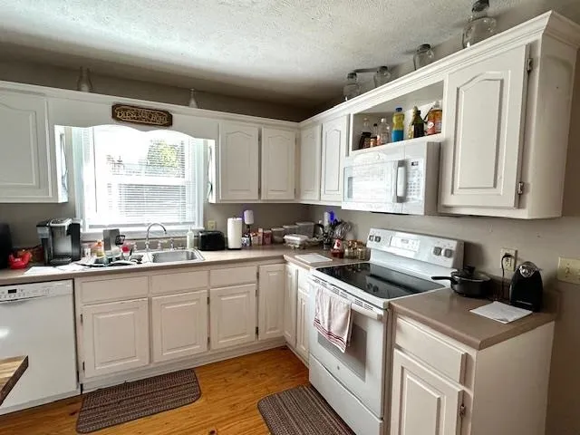 a kitchen with stainless steel appliances granite countertop a stove a sink and white cabinets with wooden floors