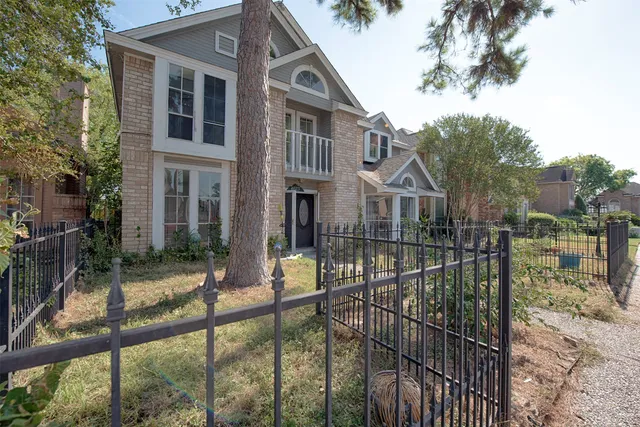 a view of a brick house that has large tree and windows