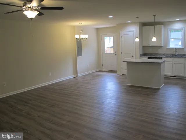 an empty room with wooden floor and kitchen view