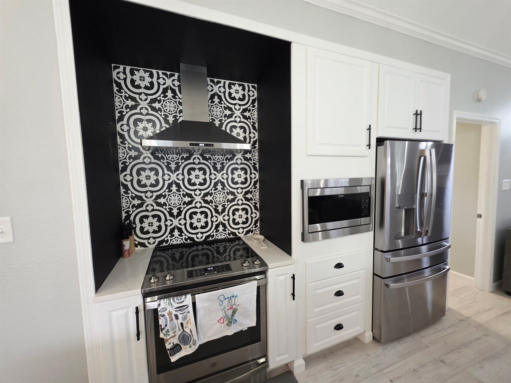 520 Red River Road Belton, TX 76513 - Photo 22 of 36 Kitchen featuring a patterned tile backsplash, stainless steel appliances, white cabinetry, integrated microwave, and a modern range hood