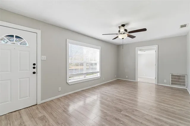 an empty room with wooden floor ceiling fan and windows