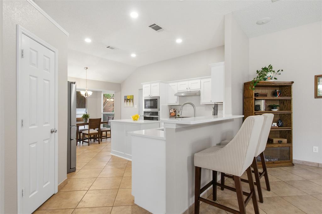 4218 Glistening Spring Rowlett, TX 75088 - Photo 10 of 39 Open-concept kitchen featuring white cabinetry, stainless steel appliances, a breakfast bar, recessed lighting, and tile flooring