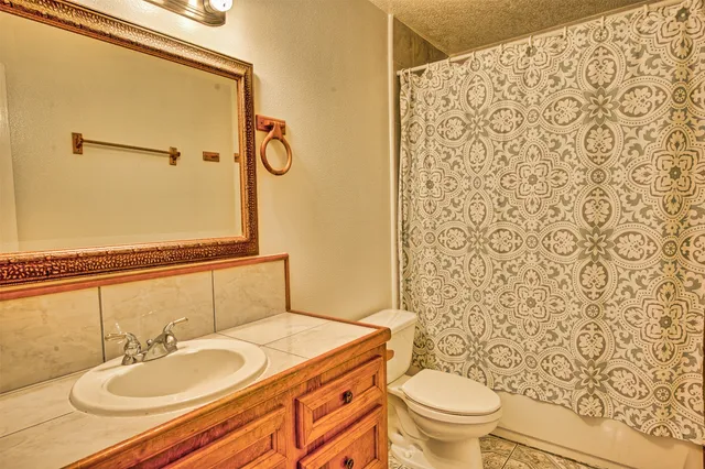 an empty room with a chandelier fan and kitchen view