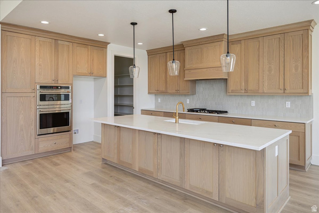 952 Mathilda Drive, Unit 156 Saratoga Springs, UT 84045 - Photo 9 of 25 Kitchen featuring light wood-finish cabinetry, a central island with a white countertop and integrated sink, stainless steel built-in double ovens, a gas range with a custom hood, and pendant lighting