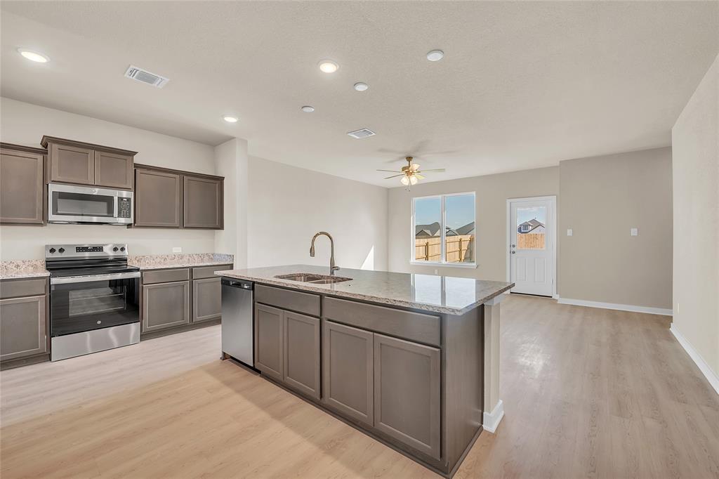 262 Boatright Boulevard Jarrell, TX 76537 - Photo 27 of 30 Kitchen with appliances with stainless steel finishes, a kitchen island with sink, light stone counters, light wood-type flooring, and open floor plan