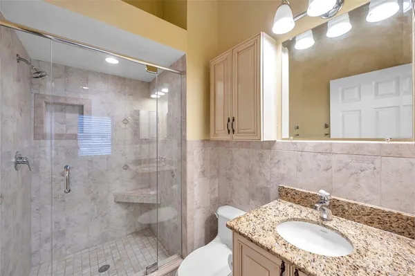 a bathroom with a granite countertop sink a toilet a mirror and shower