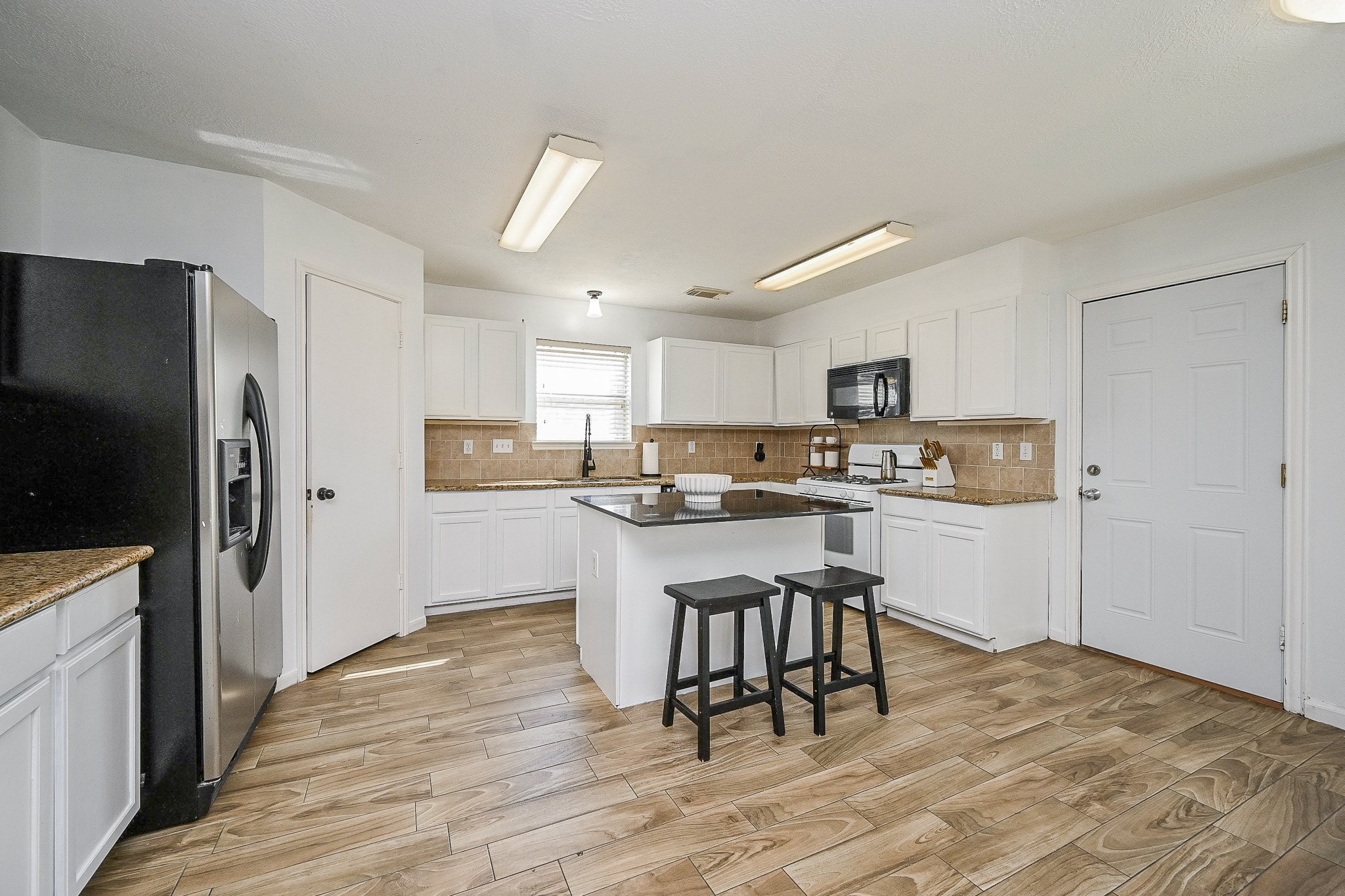 2534 Halstead Drive Spring, TX 77386 - Photo 13 of 35 This spacious kitchen boasts sleek white cabinetry, wood-look tile flooring, and a central granite topped island with seating space. Granite counters and a bright and sunny window over the sink.
