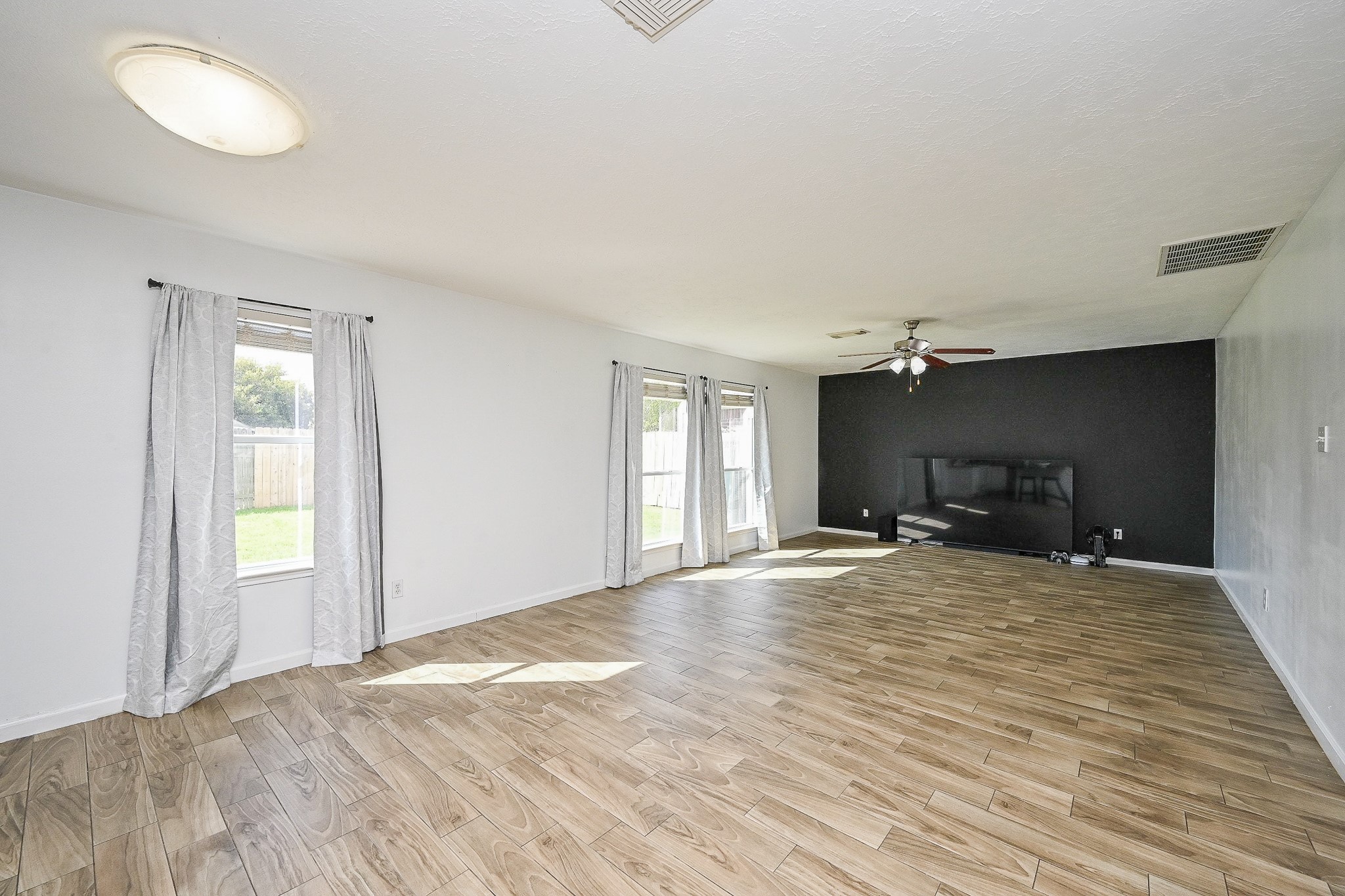 2534 Halstead Drive Spring, TX 77386 - Photo 16 of 35 Spacious living room with wood-look tile flooring, ample natural light from multiple windows, and a ceiling fan. Features a modern black accent wall ideal for entertainment setup.