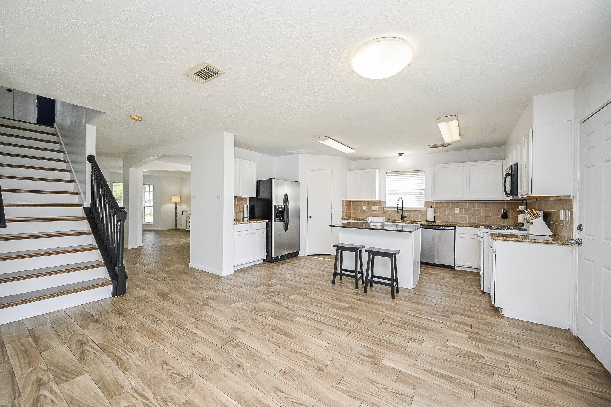 2534 Halstead Drive Spring, TX 77386 - Photo 17 of 35 This photo showcases a spacious, open-plan kitchen and dining area with , ample cabinetry, and sleek wood look -style flooring. A staircase leads to the upper level with 4 bedrooms, and there's plenty of natural light in this home!