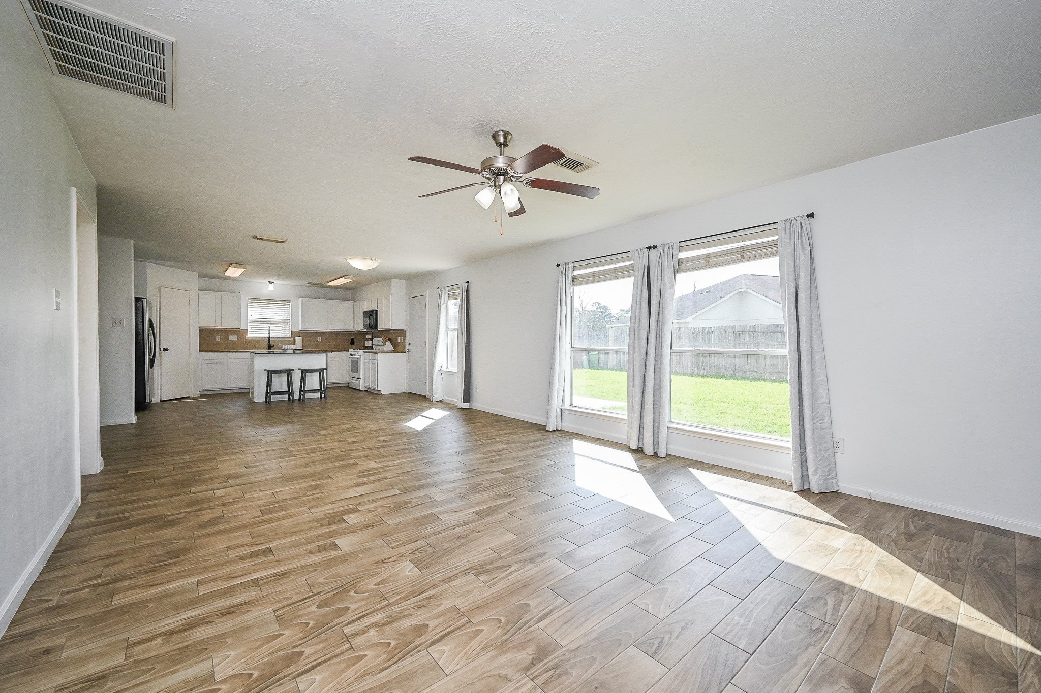 2534 Halstead Drive Spring, TX 77386 - Photo 18 of 35 A spacious and bright open-concept living area with wood-style flooring, large windows offering plenty of natural light, and a ceiling fan. It seamlessly connects to a modern kitchen with white cabinets and a central island, making it perfect for entertaining.