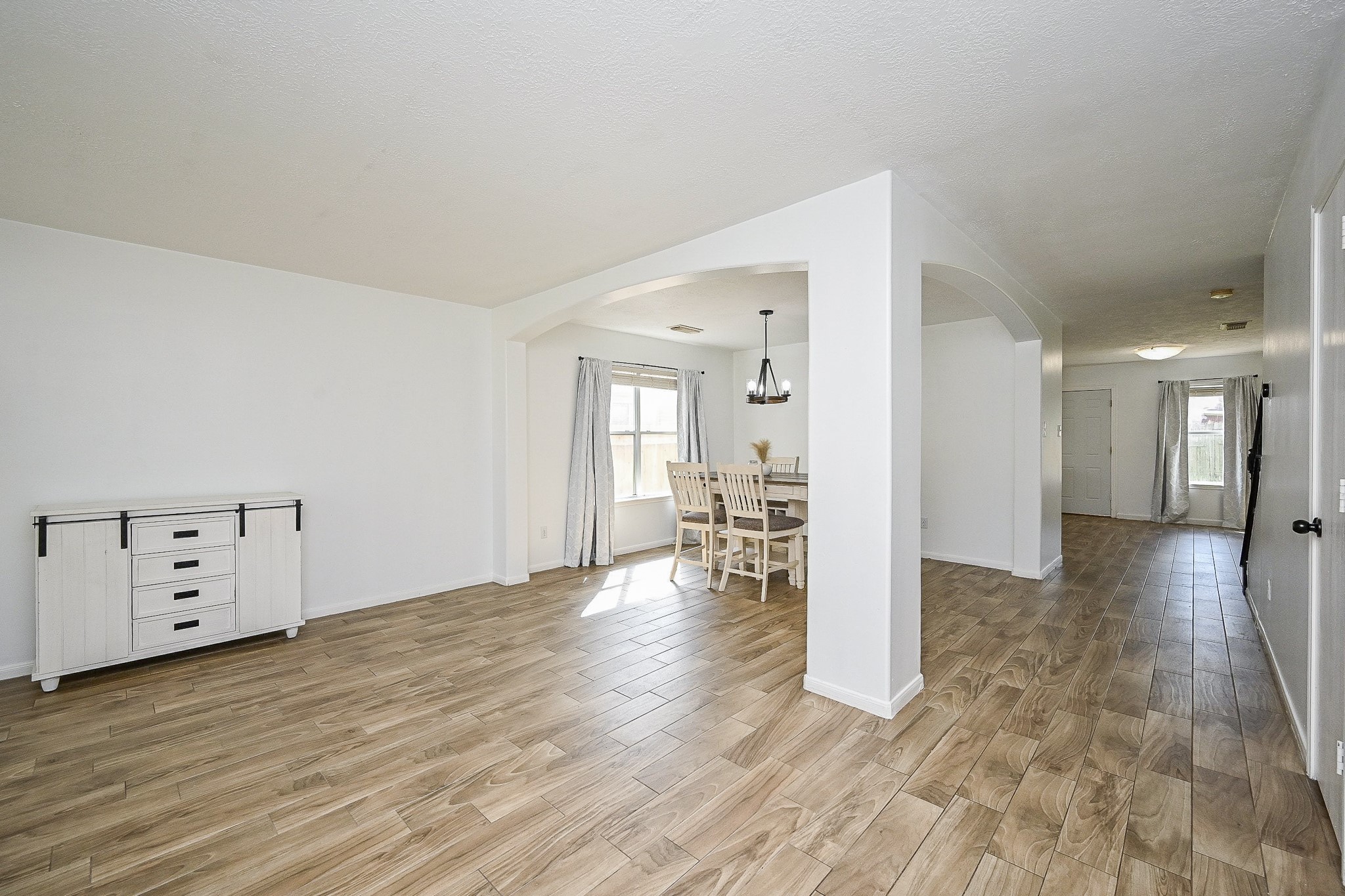 2534 Halstead Drive Spring, TX 77386 - Photo 8 of 35 This bright, open-concept living space features wood-look tile flooring and neutral walls. It includes a dining area with a modern chandelier and large windows for natural light. The room is spacious and versatile, ideal for various furniture arrangements.