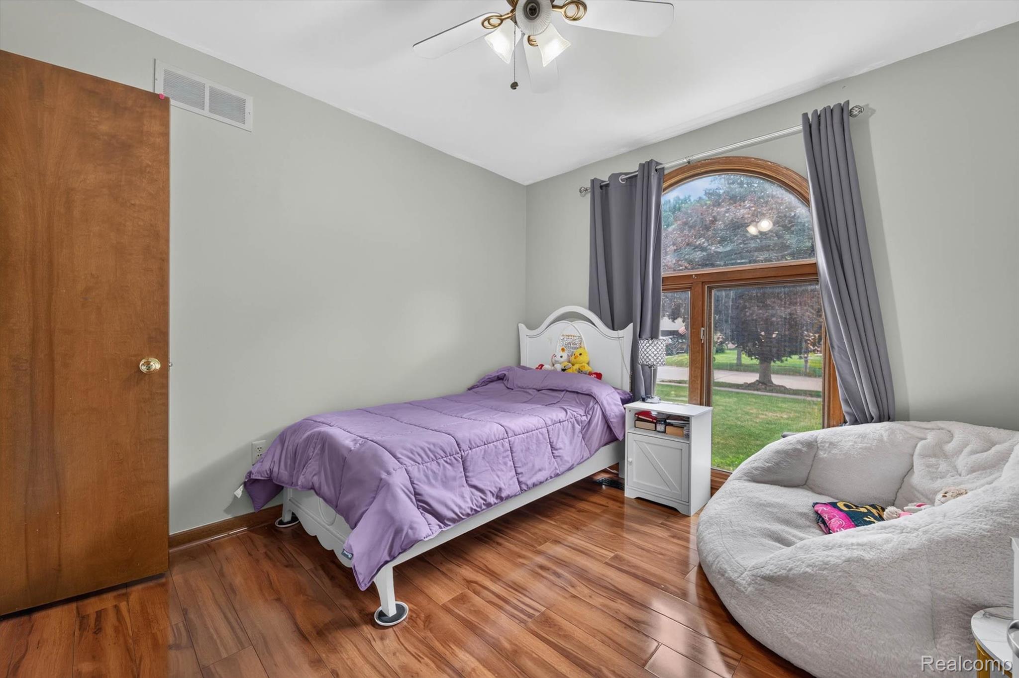 46362 Springhill Drive Utica, MI 48317 - Photo 25 of 59 Spacious room featuring wood-finish flooring, a large arched window with wood trim, a ceiling fan, light gray wall paint, and a built-in closet with a solid wood door