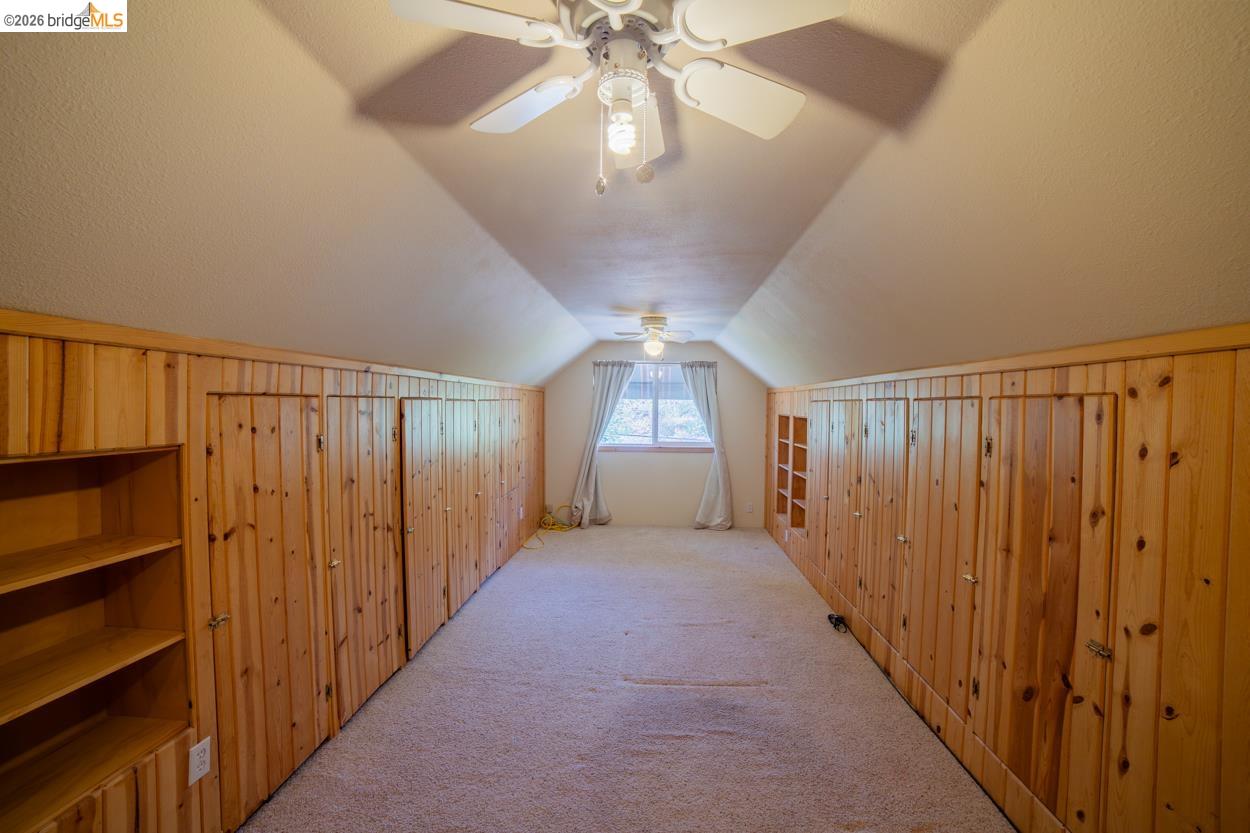 22401 Ridge Road Twain Harte, CA 95383 - Photo 24 of 52 Sloped ceiling room featuring wood-paneled walls, built-in shelving, a ceiling fan with integrated lighting, and a window with drapes