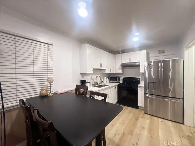 a kitchen with a refrigerator a stove a sink dishwasher a dining table and chairs with wooden floor