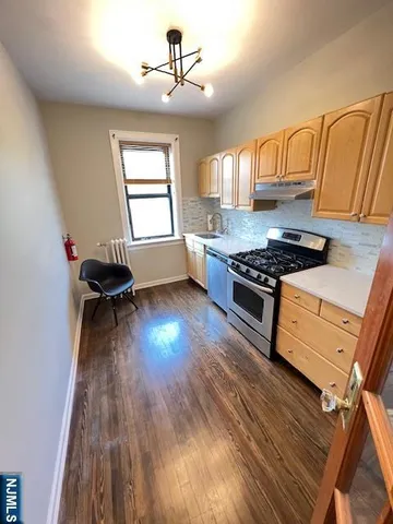 a kitchen with granite countertop a stove a chimney wooden floor and cabinets