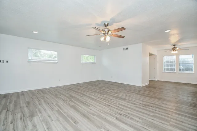 an empty room with wooden floor ceiling fan and window