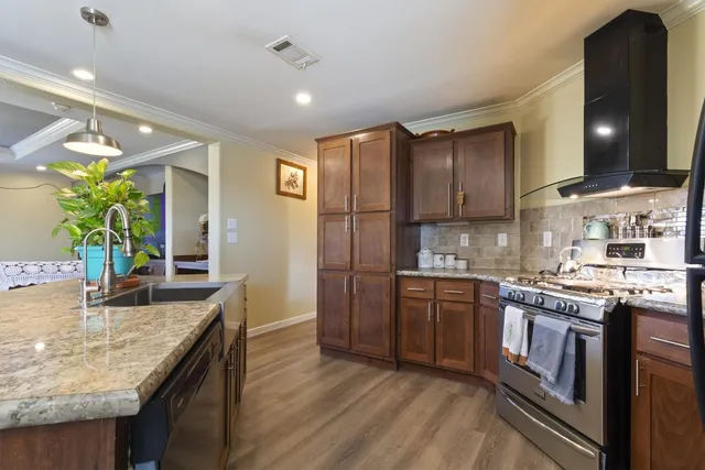 a kitchen with stainless steel appliances granite countertop wooden cabinets a stove a sink and a wooden floors