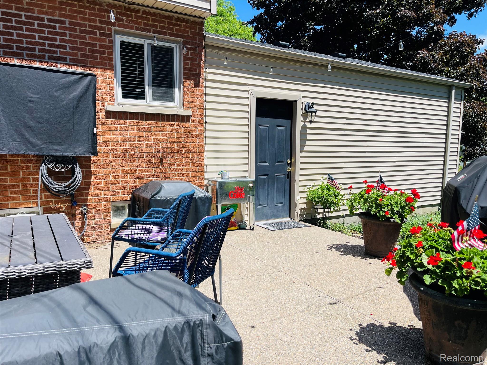 488 Welch Road Northville, MI 48167 - Photo 16 of 22 Concrete patio area with brick and siding exterior walls, featuring a window with blinds, an exterior door, and an exterior wall light fixture