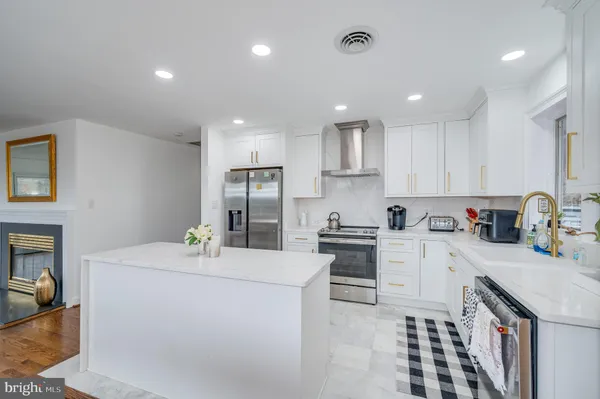 a large white kitchen with stainless steel appliances granite countertop a refrigerator a stove and a sink with wooden floor