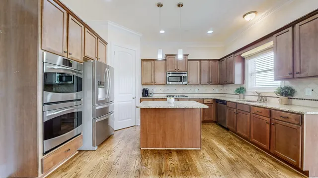 a kitchen with stainless steel appliances granite countertop a refrigerator a stove and a sink with wooden floor