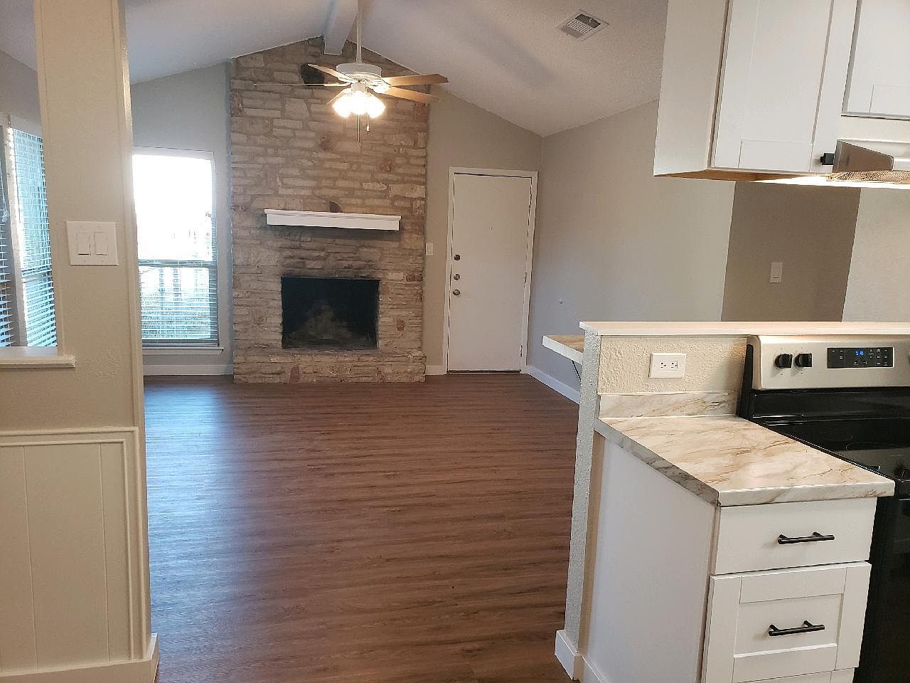 A stone fireplace anchors this inviting living space, complete with vaulted ceilings and wood-style flooring.