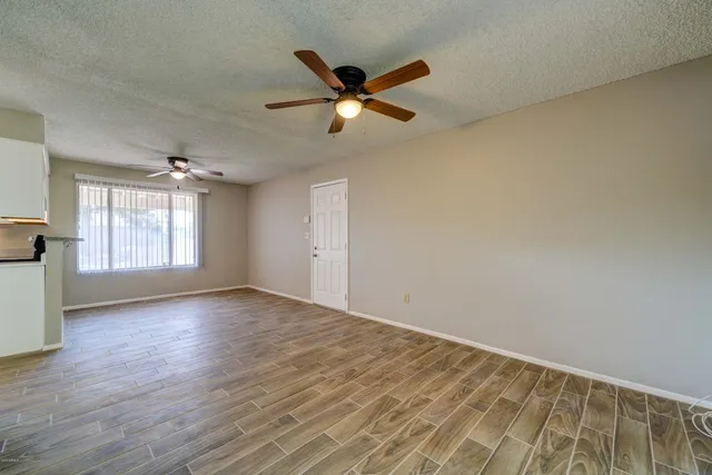 an empty room with wooden floor fan and windows