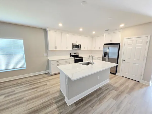a large white kitchen with wooden floor and stainless steel appliances