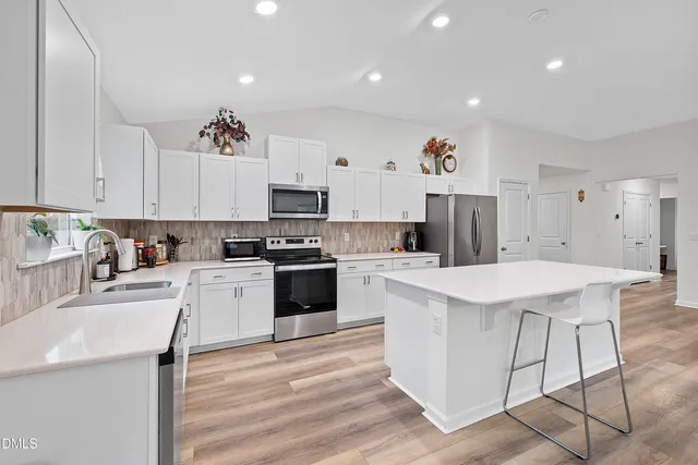 a kitchen with stainless steel appliances kitchen island granite countertop a stove a sink a refrigerator and white cabinets with wooden floor