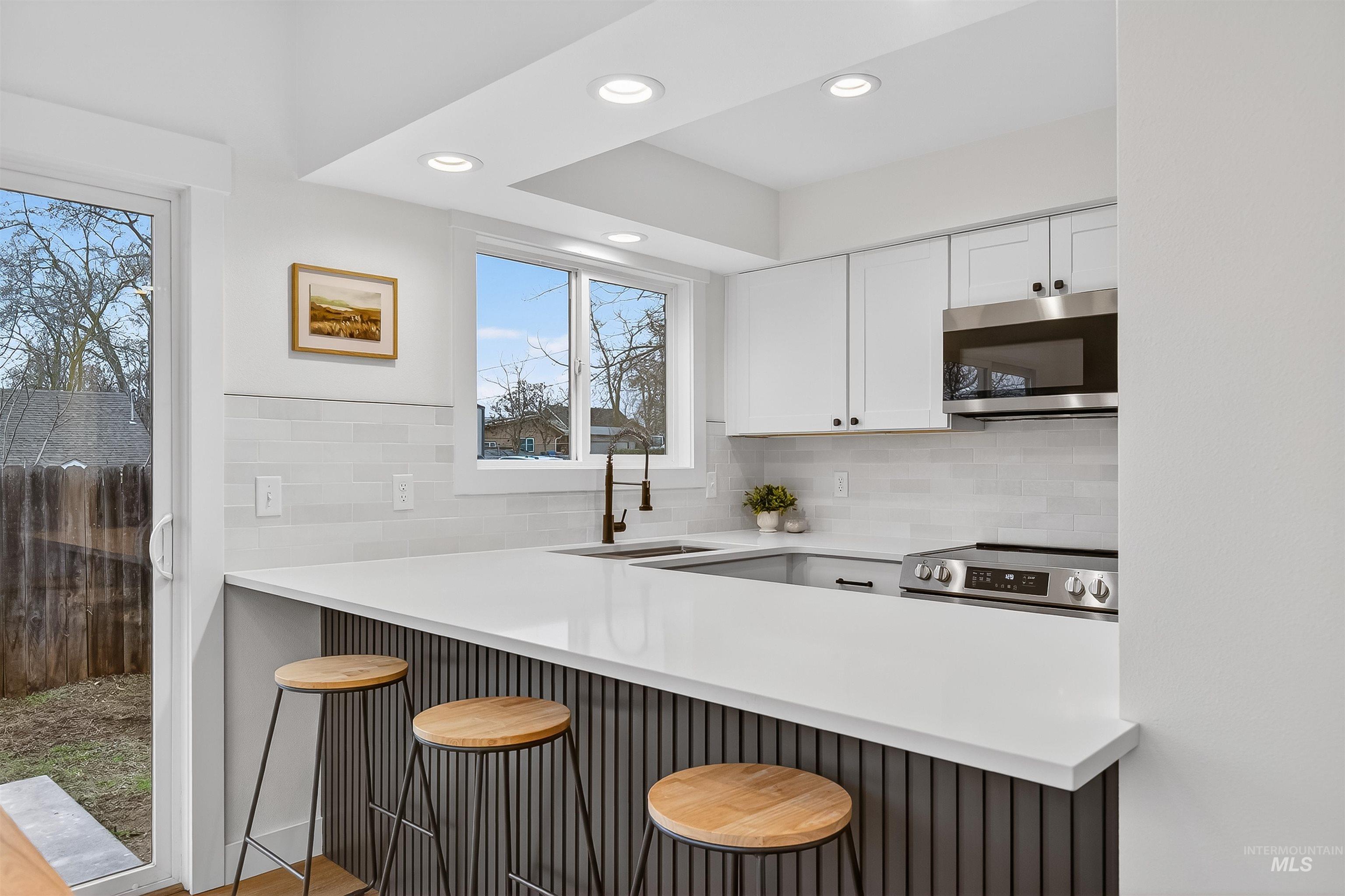 Kitchen featuring appliances with stainless steel finishes, white cabinets, a kitchen breakfast bar, tasteful backsplash, and recessed lighting
