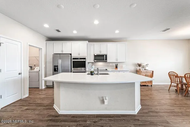a view of kitchen center island stainless steel appliances wooden floor and living room view