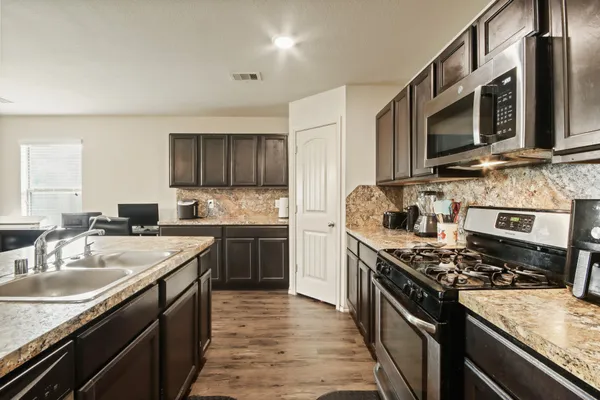 a kitchen with stainless steel appliances granite countertop a stove top oven a sink dishwasher and a microwave oven with white cabinets