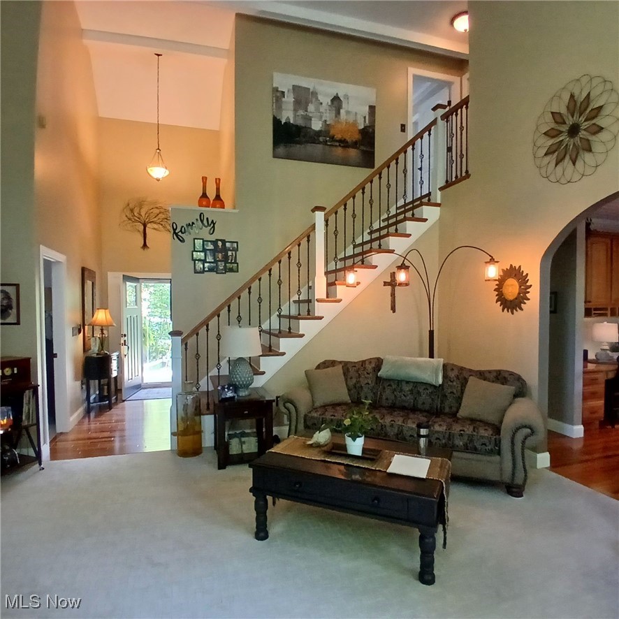 5232 Emerson Road Madison, OH 44057 - Photo 3 of 48 Carpeted living room featuring stairway, arched walkways, a towering ceiling, and wood finished floors