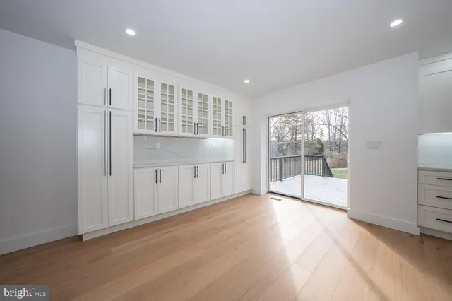 a view of an empty room with wooden floor and a kitchen