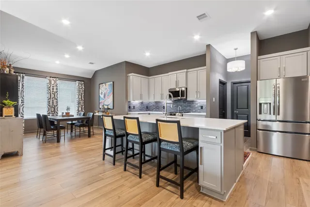 a kitchen with stainless steel appliances granite countertop a refrigerator a stove a sink a dining table and chairs with wooden floor