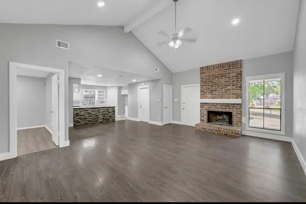 a view of an empty room with wooden floor fireplace and a window