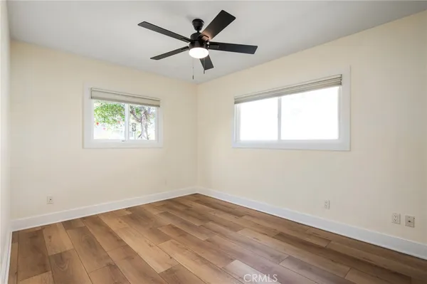 an empty room with wooden floor fan and windows