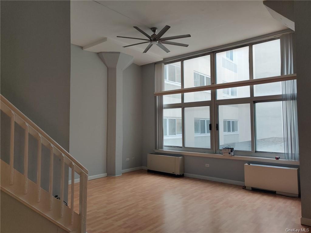 a view of an empty room with windows & a ceiling fan