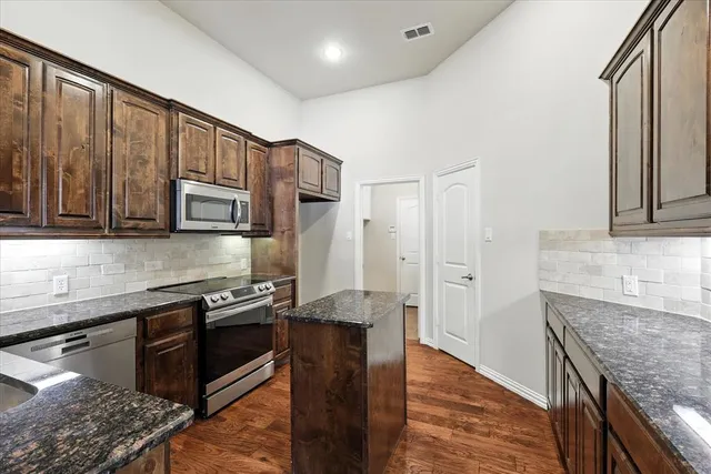 a kitchen with stainless steel appliances granite countertop a stove top oven a sink dishwasher and wooden cabinets with wooden floor