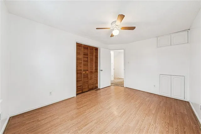 a view of an empty room with wooden floor and a ceiling fan